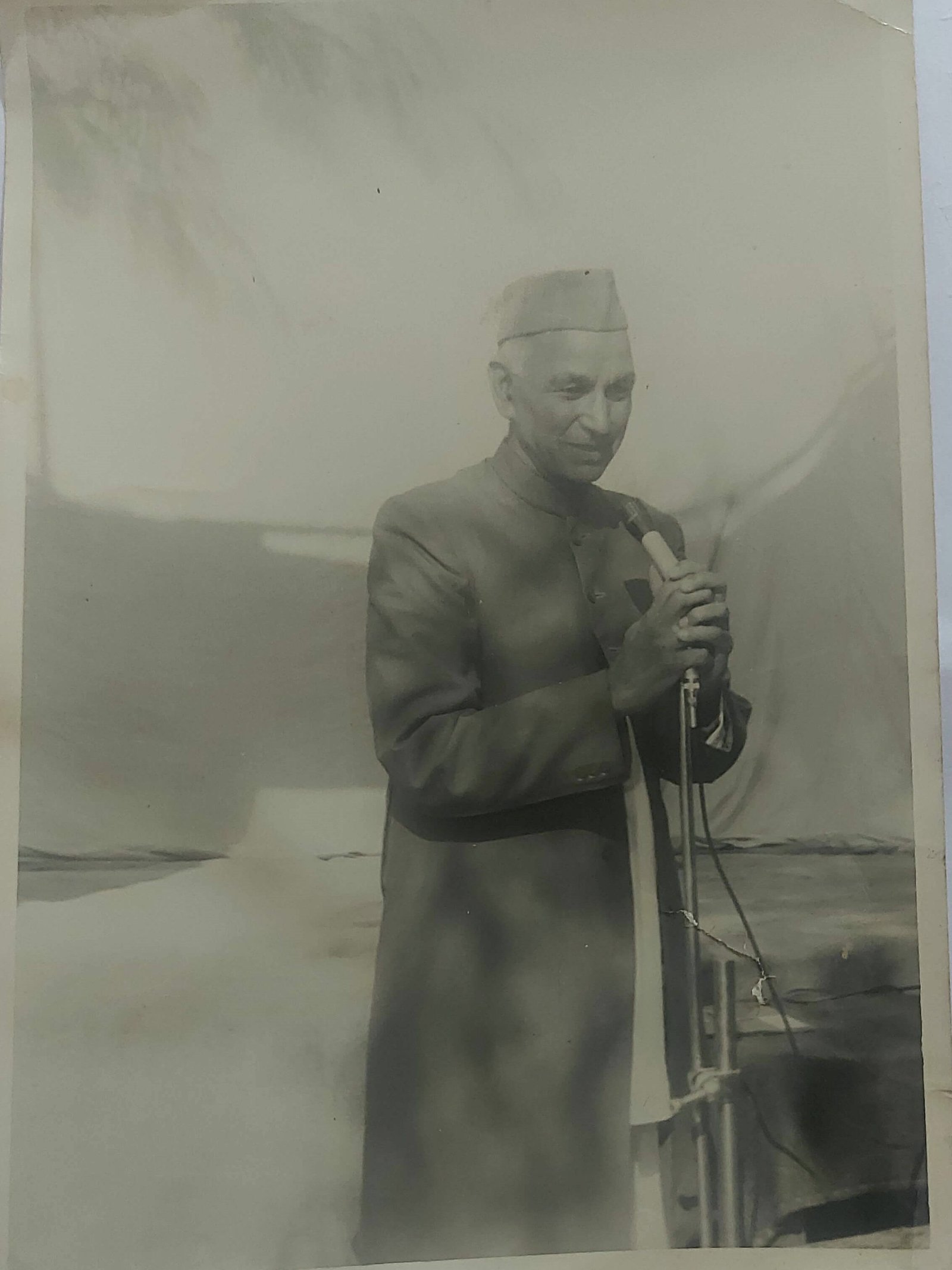 A man in a Gandhi cap speaking at a microphone at a school function