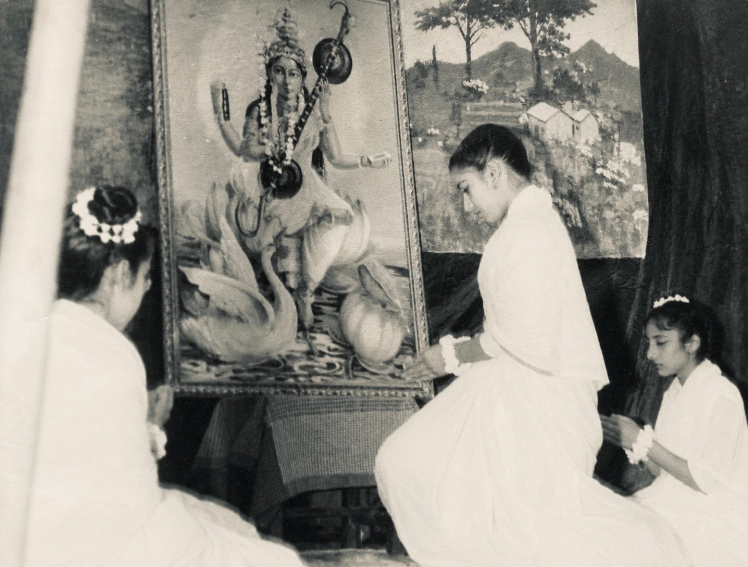 Girls in white performing the Saraswati pooja before the framed painting of the Goddess on the annual-day stage, 1964