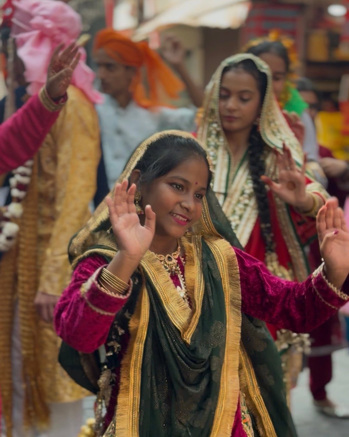 A young student in a maroon velvet suit and green and gold dupatta dancing in the procession