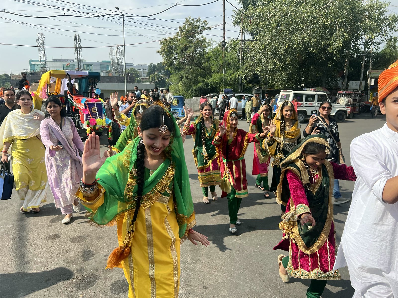 A student in a yellow suit and green dupatta waving as the procession moves through the city