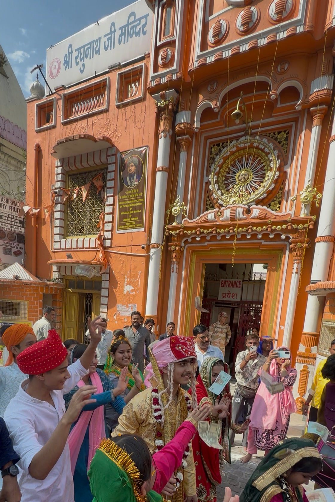 The baraat dancing in front of Shri Raghunath Ji Mandir, with the groom at the centre and onlookers filming