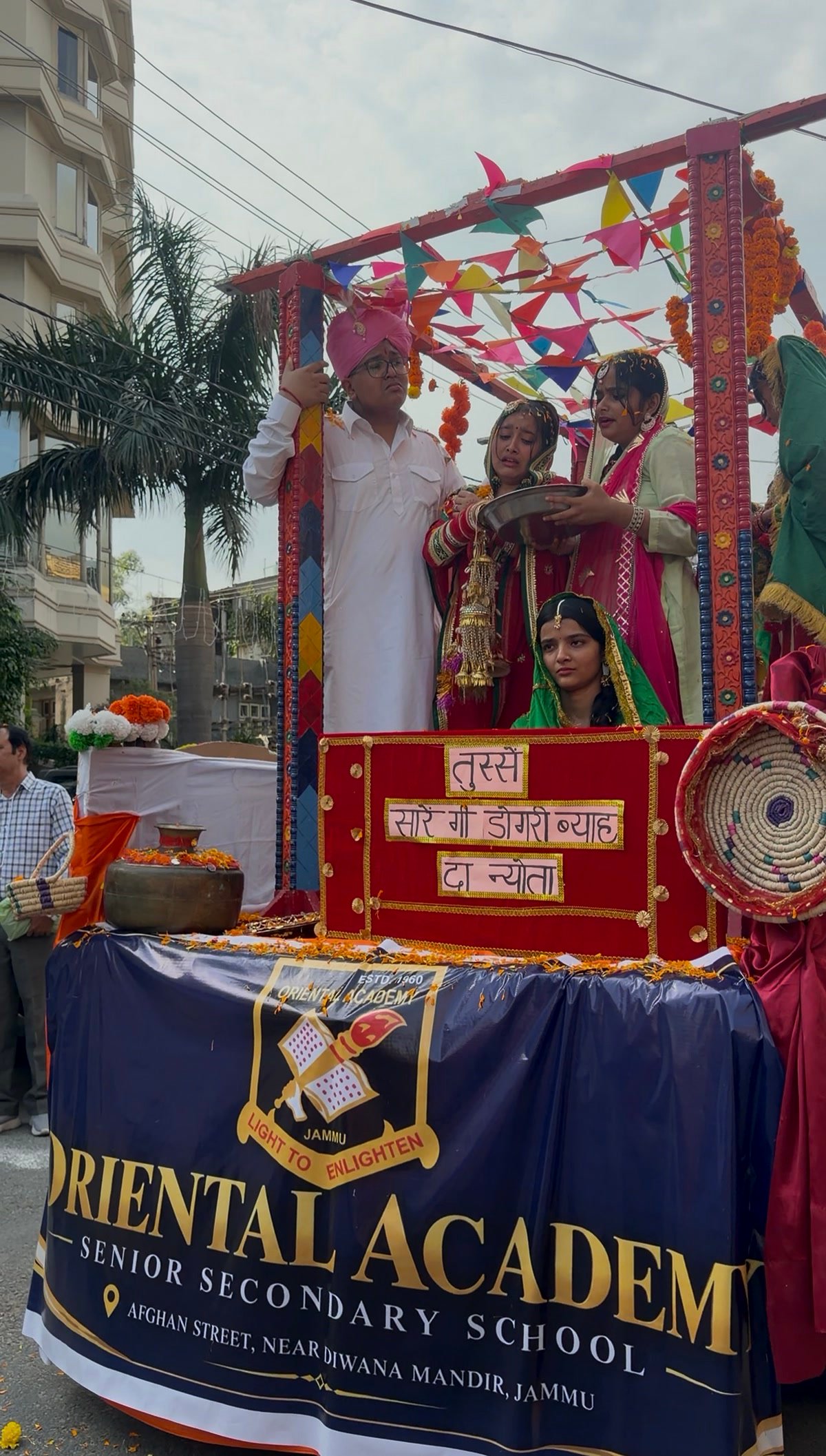 The wedding tableau on a decorated cart, with a red Dogri sign and the Oriental Academy banner across the front