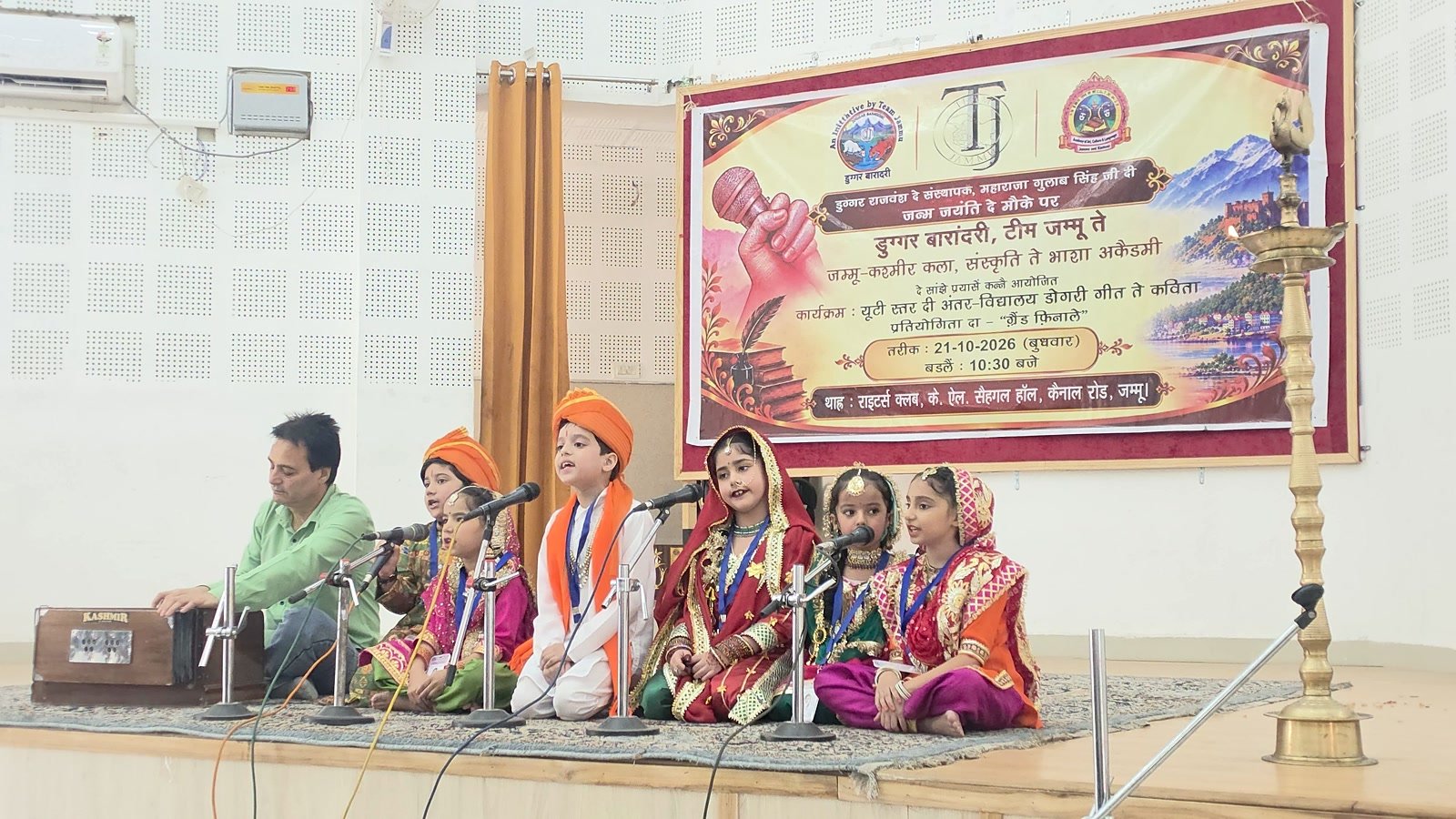 A group of Oriental Academy students singing on stage, accompanied on the harmonium