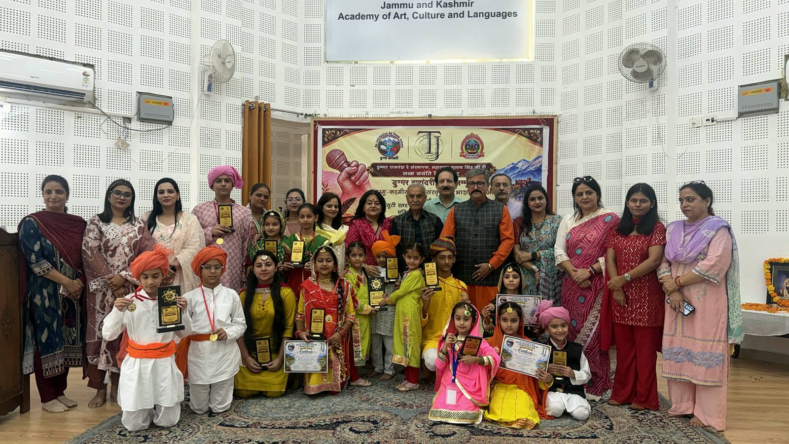 Oriental Academy students in traditional Dogra dress with their teachers and the guests, on stage in front of the competition banner