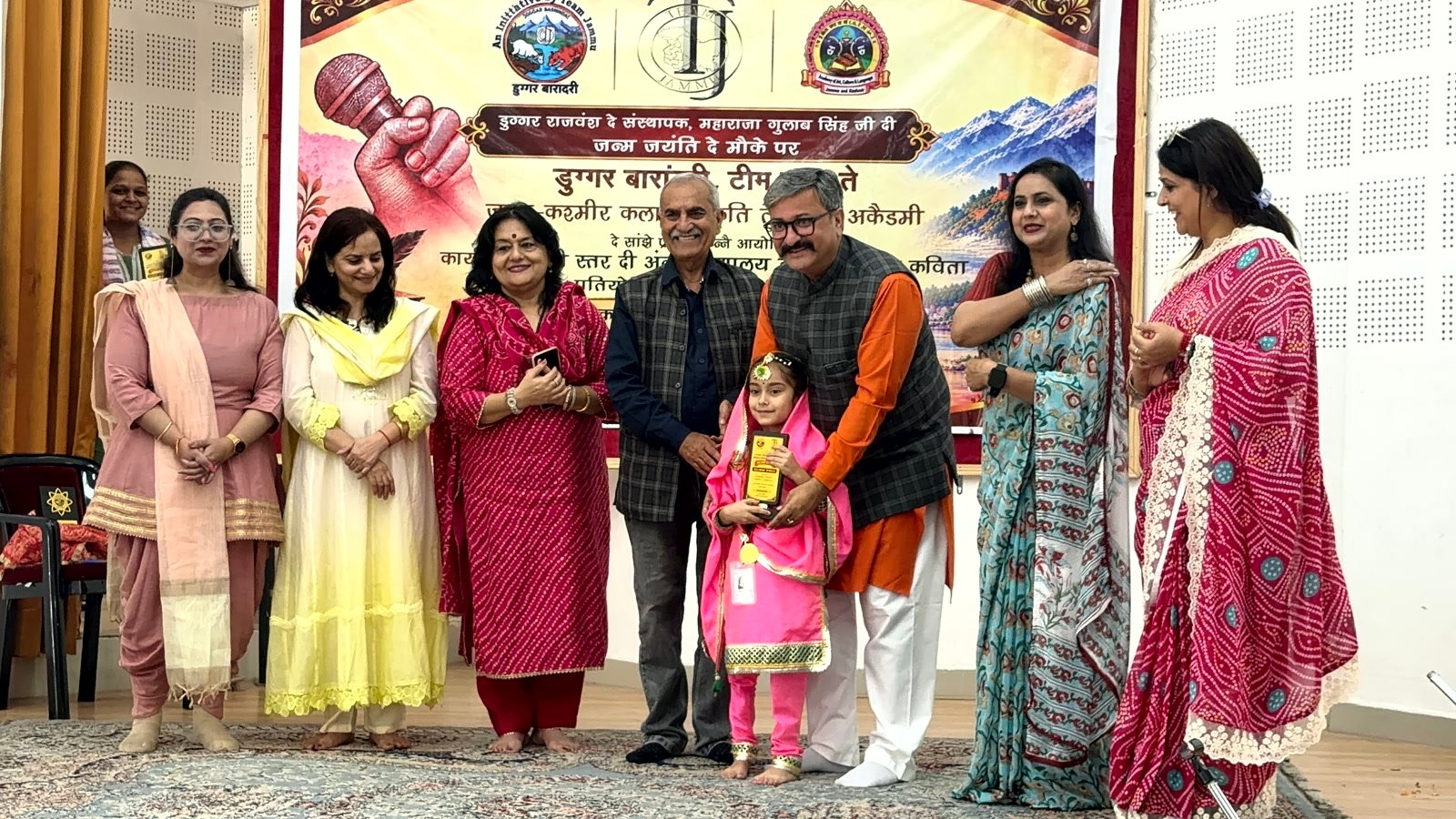 Kyra Jamwal, in a pink suit, receiving her trophy from the guests on stage