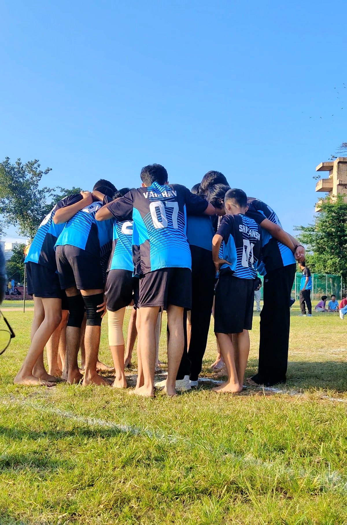 Players in a team huddle on the field, arms around each other