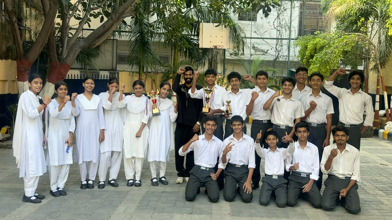 Both teams in school uniform cheering with their trophies in the school courtyard