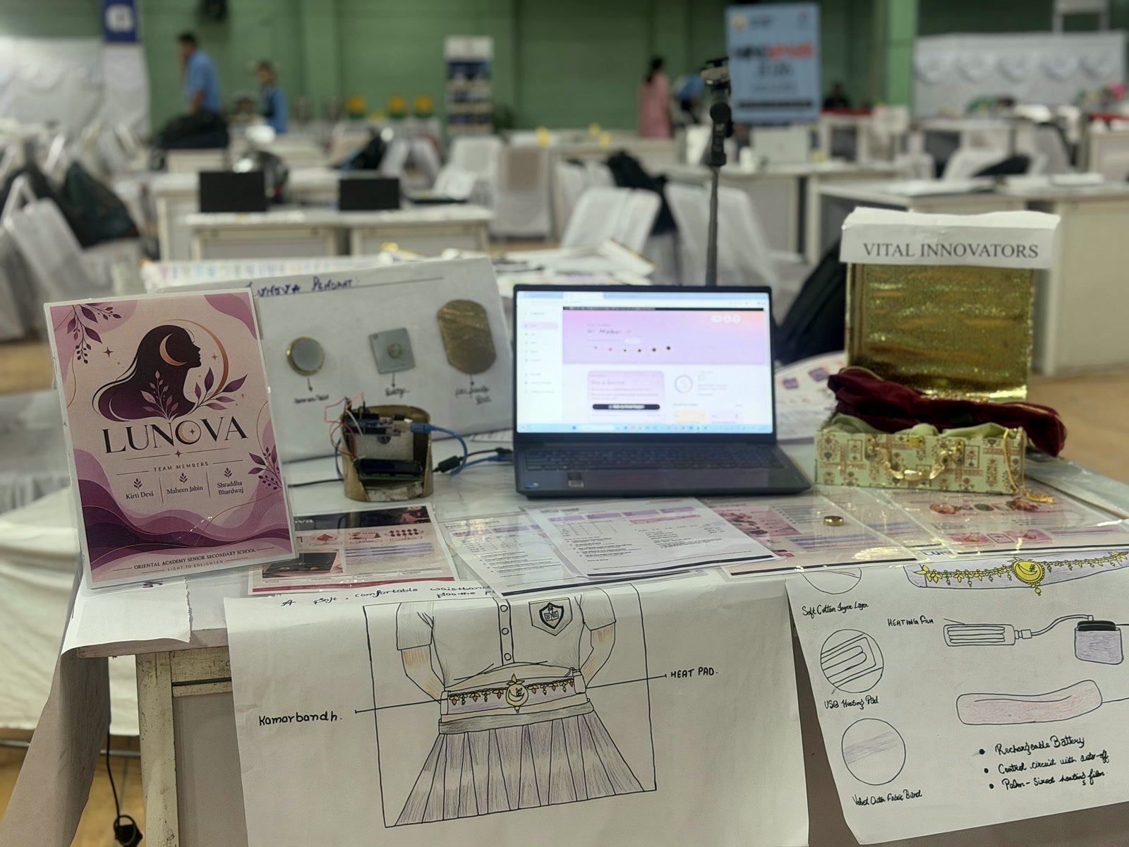 The Lunova stall: the Lunova team card, the jewellery display, the app on a laptop and design sketches of a heat band