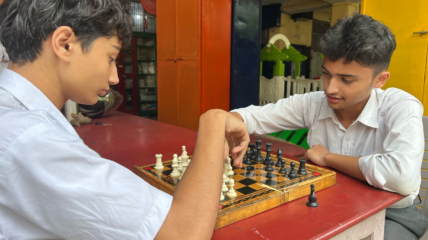 Two senior boys in white school shirts playing chess on a wooden board
