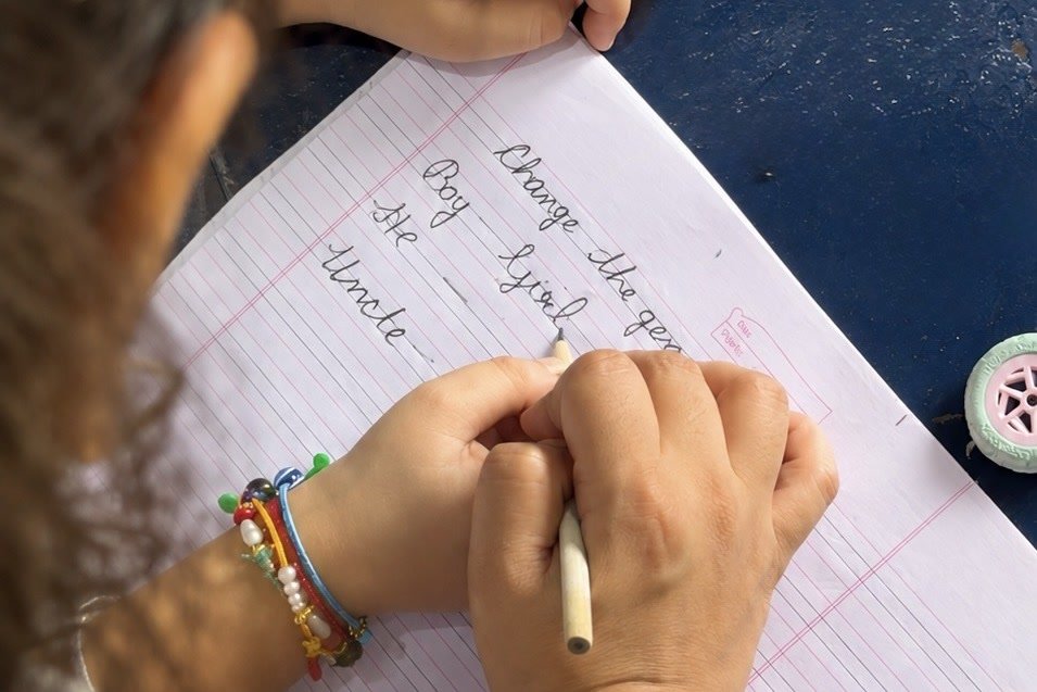A young student practising cursive in an exercise book, writing out Change the gender: Boy, Girl, He, Uncle