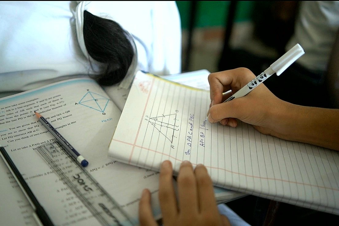 A senior student working through a geometry problem in a notebook, a ruler and a pen on the desk