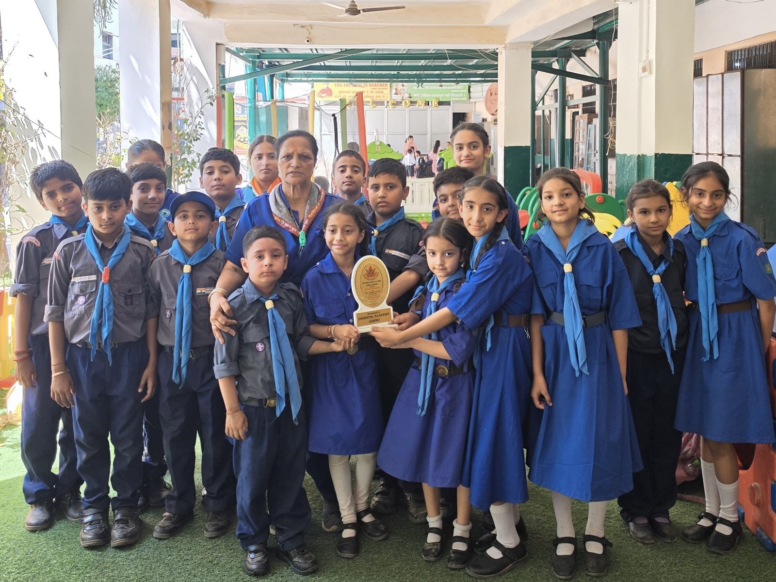 Oriental Academy Cubs and Bulbuls in uniform with their teacher, two of them holding a trophy whose plaque reads Presented to Oriental Academy Jammu