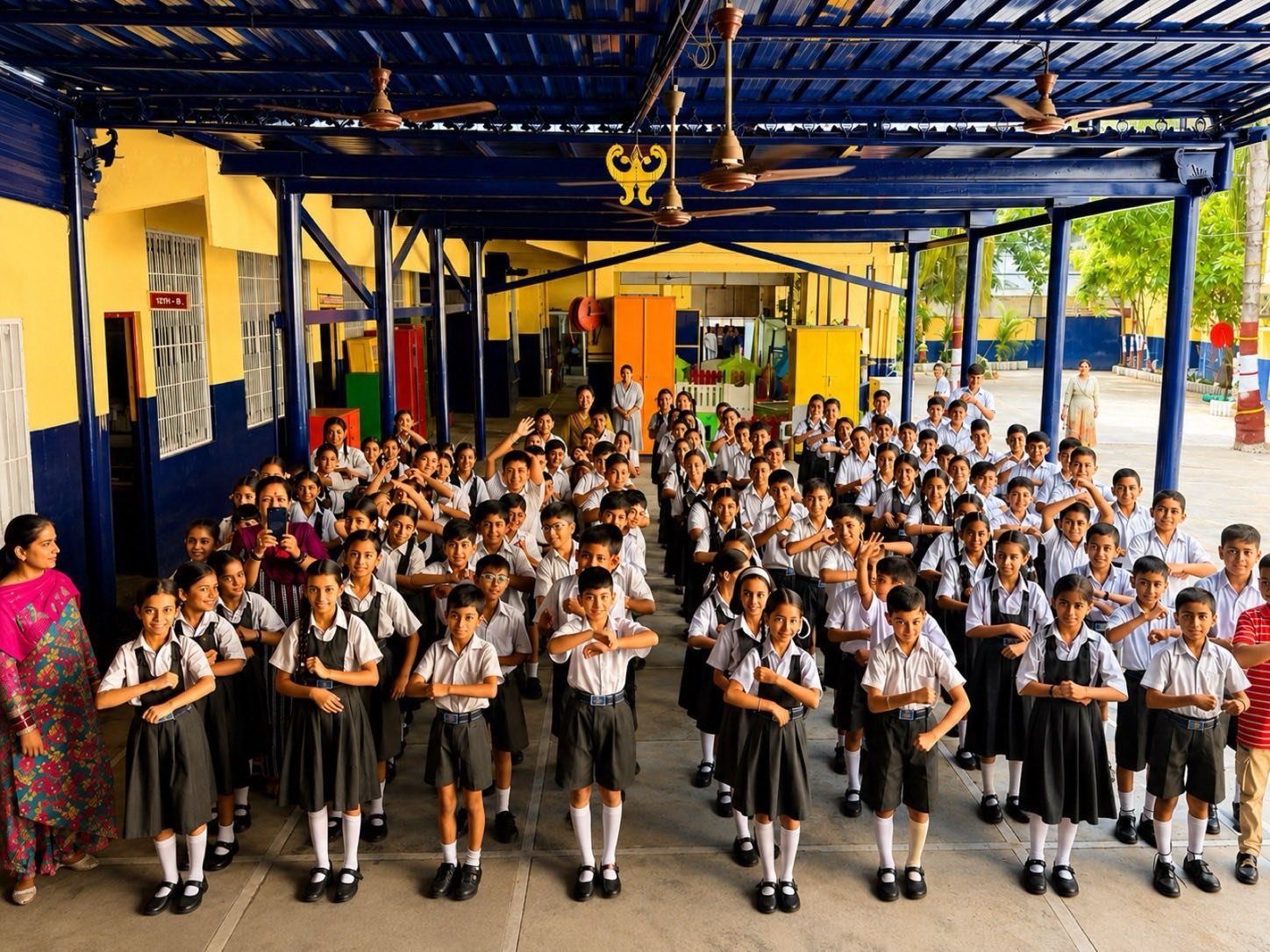 Students standing in rows at morning assembly in the covered courtyard, with their teachers beside them
